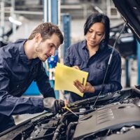 Auto car repair service center. Two mechanics - man and woman examining car engine