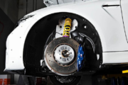 Close-up of a car's suspension system with visible yellow coilover and blue brake caliper.