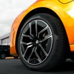 A sleek orange car fitted with stylish auto tires and modern alloy wheels, emphasizing both performance and design.